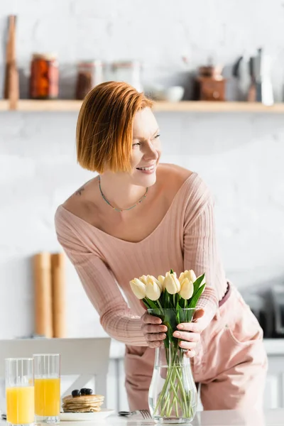 Happy Redhead Woman Putting Tulips Vase Orange Juice Pancakes Table — Stock Photo, Image