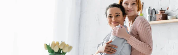 Happy Interracial Lesbian Couple Looking Camera Tulips Blurred Foreground Banner — Stock Photo, Image