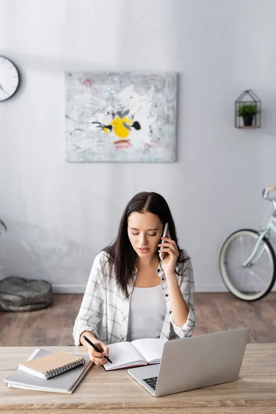 Junge Freiberuflerin Spricht Mit Handy Und Schreibt Notizbuch Neben Laptop — Stockfoto