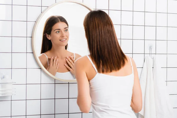バスルームで鏡を見ながら完璧な肌の笑顔を持つ幸せな女性 — ストック写真