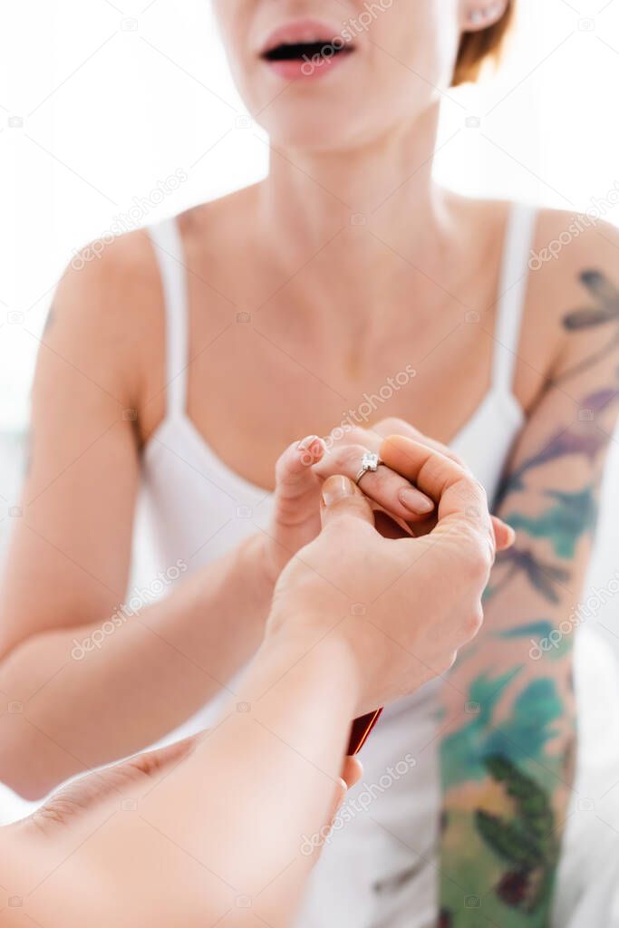cropped view of lesbian woman putting wedding ring on finger of amazed tattooed girlfriend, blurred background