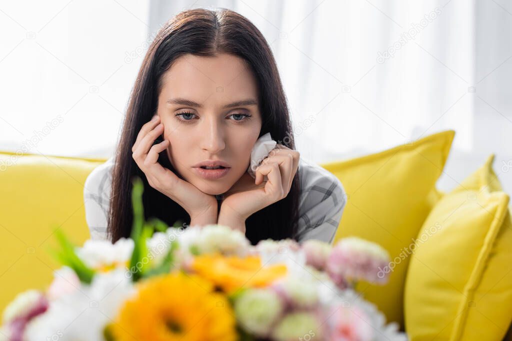 upset allergic woman holding paper napkin near flowers on blurred foreground