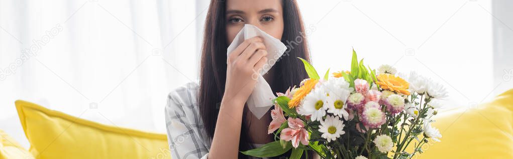 allergic woman wiping nose with paper napkin near flowers, banner
