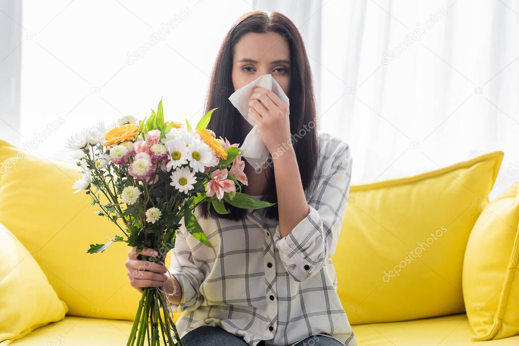 young woman holding flowers and suffering from allergy at home