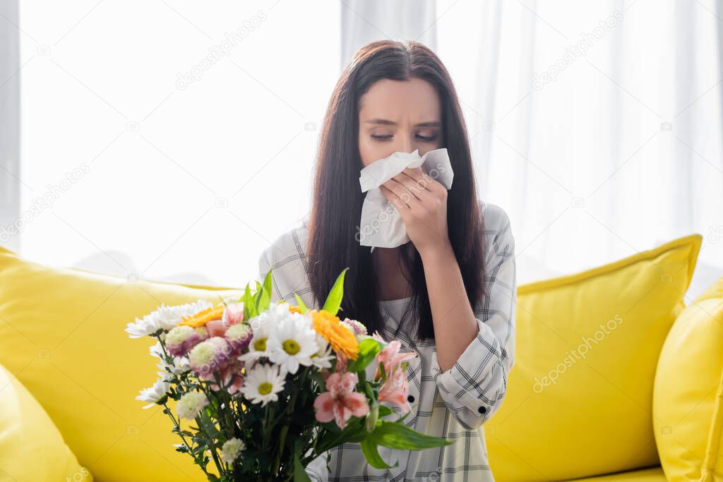 allergic woman wiping nose with paper napkin while sitting near flowers