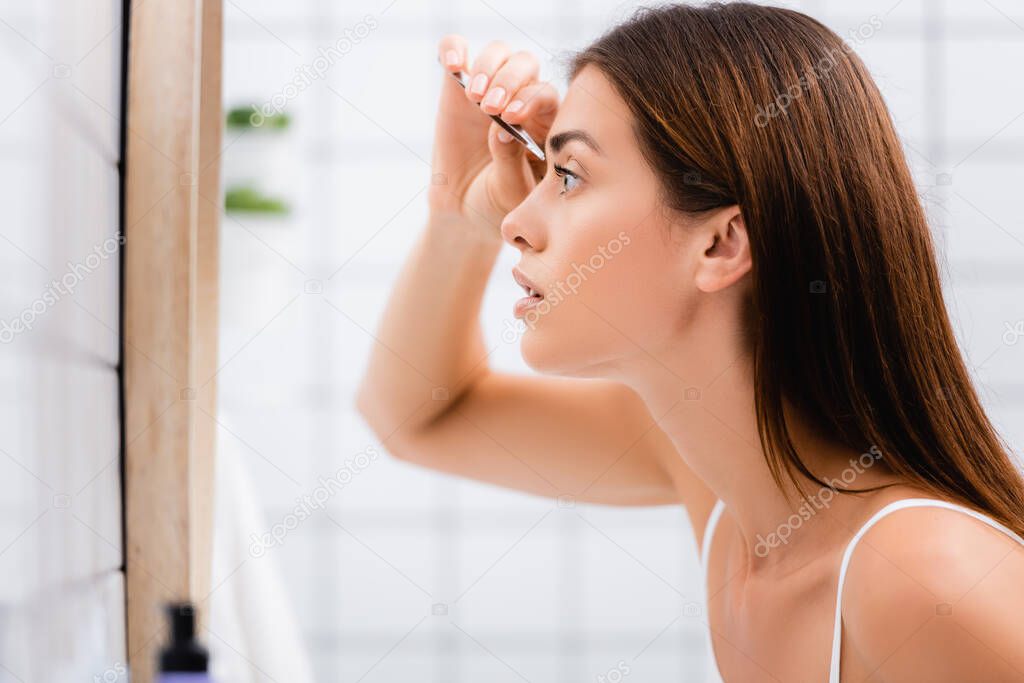 side view of young woman tweezing eyebrows in bathroom