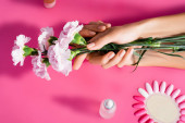 oříznutý pohled na ženu držící karafiáty květiny v blízkosti palety umělých nehtů a odstraňovač kůžičky na růžovém pozadí