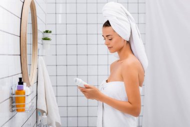 young woman with white towel on head holding deodorant in bathroom clipart