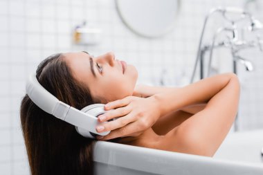 Banyo yaparken ve müzik dinlerken kablosuz kulaklıklara dokunan genç bir kadın.