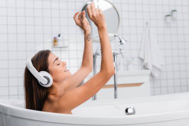 Kablosuz kulaklıkla müzik dinlerken banyo yapan gülümseyen kadın.