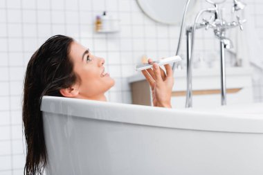 Banyo yaparken cep telefonuyla konuşan neşeli kadın.