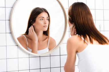 young woman in white undershirt looking in mirror in bathroom clipart