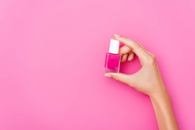 Pembe arka planda parlak tırnak cilası olan bakımlı kadın elinin üst görüntüsü.