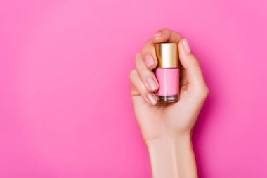 Pembe arka planda pastel oje şişesiyle tımarlanmış kadın elinin üst görüntüsü.