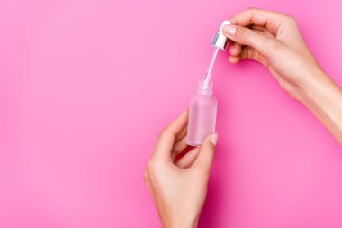 Pembe arka planda elinde damlatan ve bir şişe tırnak eti çıkarıcı tutan kadının kısmi görüntüsü