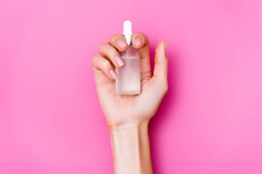 Pembe arka planda bir şişe tırnak törpüsü ile tımarlanmış kadın elinin üst görüntüsü.
