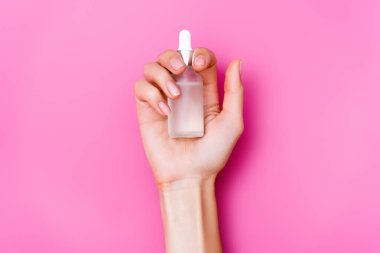 top view of groomed female hand with bottle of cuticle remover on pink background clipart