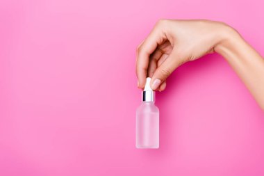 Pembe arka planda tırnak eti sökücü şişesi olan kadının kısmi görüntüsü