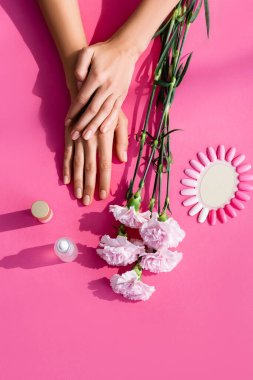 top view of female hands near carnation flowers, palette of artificial nails, cuticle remover and nail polish on pink background clipart