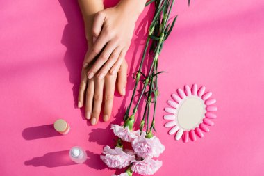 top view of female hands near palette of fake nails, carnation flowers, cuticle remover and nail varnish on pink background clipart