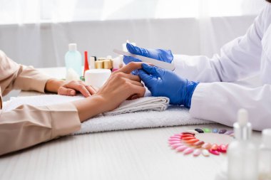 Manikürcünün tırnak törpüsü tutarken ön planda bulanık manikür yaptığı görüntüler