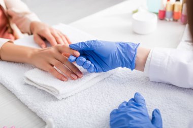 Lastik eldivenli manikürcünün müşterinin parmağına dokunuşu.