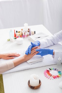 Bulanık arka planda tırnak cilası şişelerinin yakınındaki müşterinin manikürcüye dokunuşunun kısmi görünümü