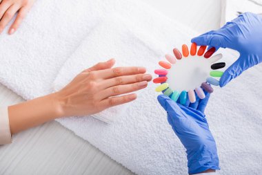 Müşterinin elinin yanında renkli yapay çivi örnekleri tutan manikürcülerin kısmi görüntüsü