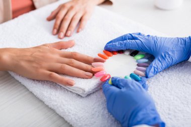 Manikürcünün elinde, müşterinin elinin yanında renkli yapay tırnaklar bulunan görüntüsü bulanık arkaplan