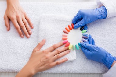 cropped view of manicurist holding palette of multicolored fake nails near client  clipart