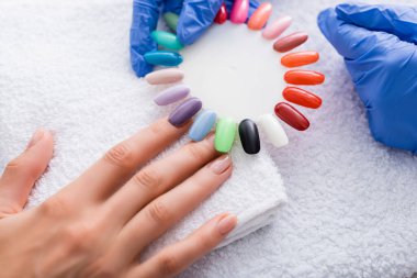 partial view of manicurist holding set of multicolored false nails near hand of client clipart