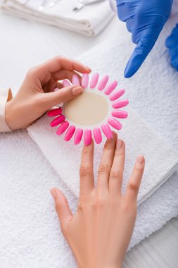 partial view of manicurist pointing with finger at samples of artificial nails in hand of client clipart