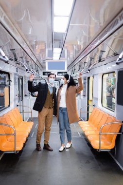 Tıbbi maskeli ırklar arası bir çift ve metroda kablosuz kulaklık.