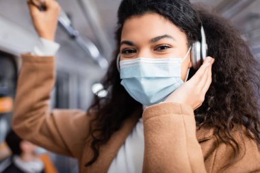 Tıbbi maskeli genç Afrikalı Amerikalı kadın metroda müzik dinliyor. 