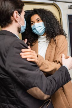 Tıbbi maskeli Afro-Amerikan kadın metroda erkek arkadaşıyla kucaklaşıyor.