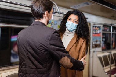 Kıvırcık Afrikalı Amerikalı kız arkadaşına sarılan, metroda maske takan bir adam. 