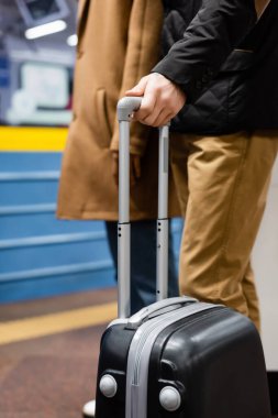 cropped view of couple standing on platform of subway with luggage  clipart