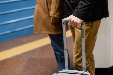 partial view of couple standing on platform of subway with luggage  clipart