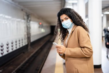 Kıvırcık Afrikalı Amerikan kadın metroda akıllı telefon tutuyor.