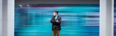 motion blur of man in medical mask standing with crossed arms near passing wagon in subway, banner clipart