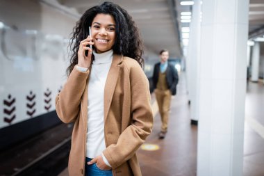 Mutlu bir Afrikalı Amerikalı kadın metroda arka planda akıllı telefondan erkeğin yanında konuşuyor. 