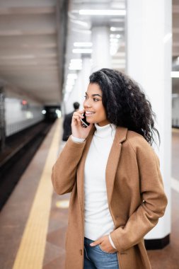 Neşeli Afrikalı Amerikalı kadın metroda arka planda akıllı telefondan konuşuyor. 