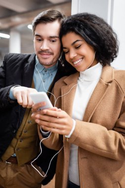 Akıllı telefona bakan ve metroda kulaklıkla müzik dinleyen mutlu çok kültürlü bir çift. 