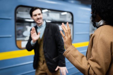 African american woman and man waving hands near wagon in metro on blurred background  clipart