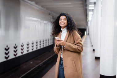 Neşeli Afrikalı Amerikalı kadın metroda akıllı telefon tutuyor. 