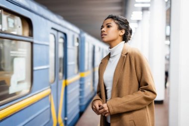 Kıvırcık Afrikalı Amerikalı kadın bulanık arka planda metro vagonuna bakıyor.