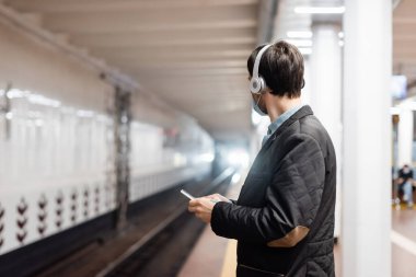 Tıbbi maskeli dövmeli adam ve metroda akıllı telefon tutan kablosuz kulaklıklı adam. 