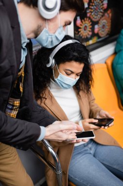 Çok kültürlü kadın ve tıbbi maskeli adam metroda akıllı telefon kullanıyor.