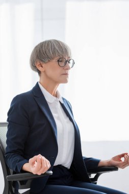 Gözlüklü orta yaşlı takım lideri ofiste meditasyon yapıyor.