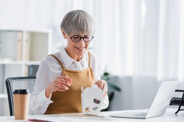 Gözlüklü mutlu takım lideri yemek paketini ofisteki karton kutuda tutuyor.